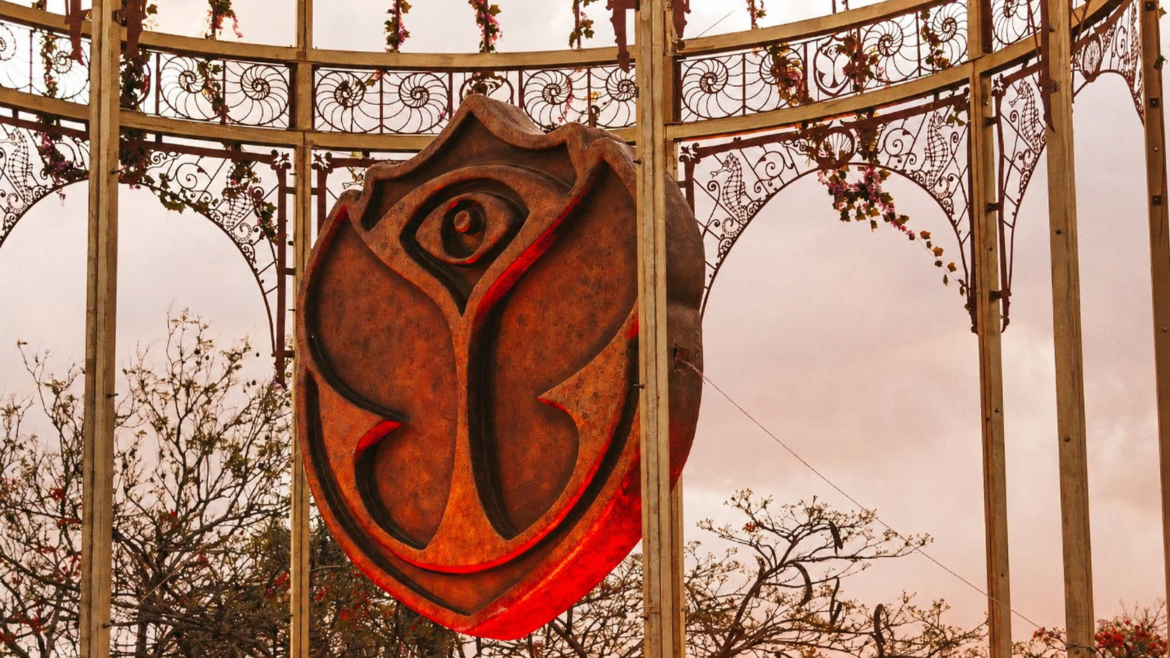 Rusty shield sculpture with a stylized rose design hanging inside ornate metal arches outdoors.