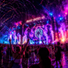 Large outdoor concert at night with colorful lights and a cheering crowd in front of a stage that reads 'Music Unites Us'.